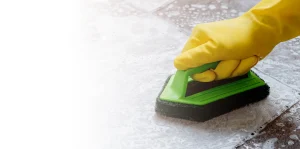 A gloved hand using a scourer to deep clean floor tiles