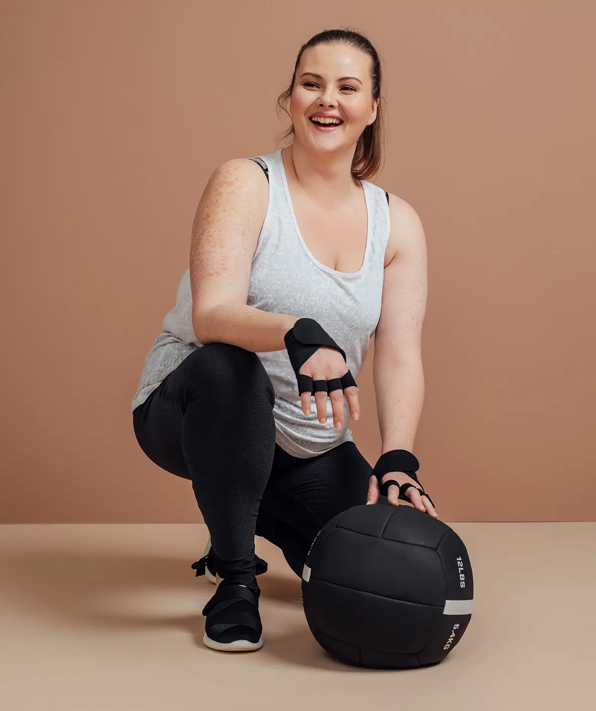 A person dressed in gym clothes kneeling on the floor with a ball